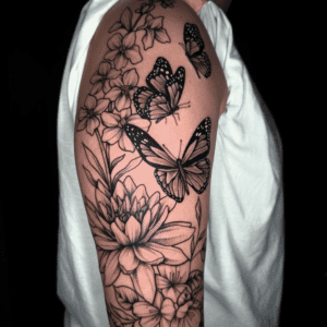 A detailed black-and-grey upper arm tattoo of butterflies and blooming flowers.